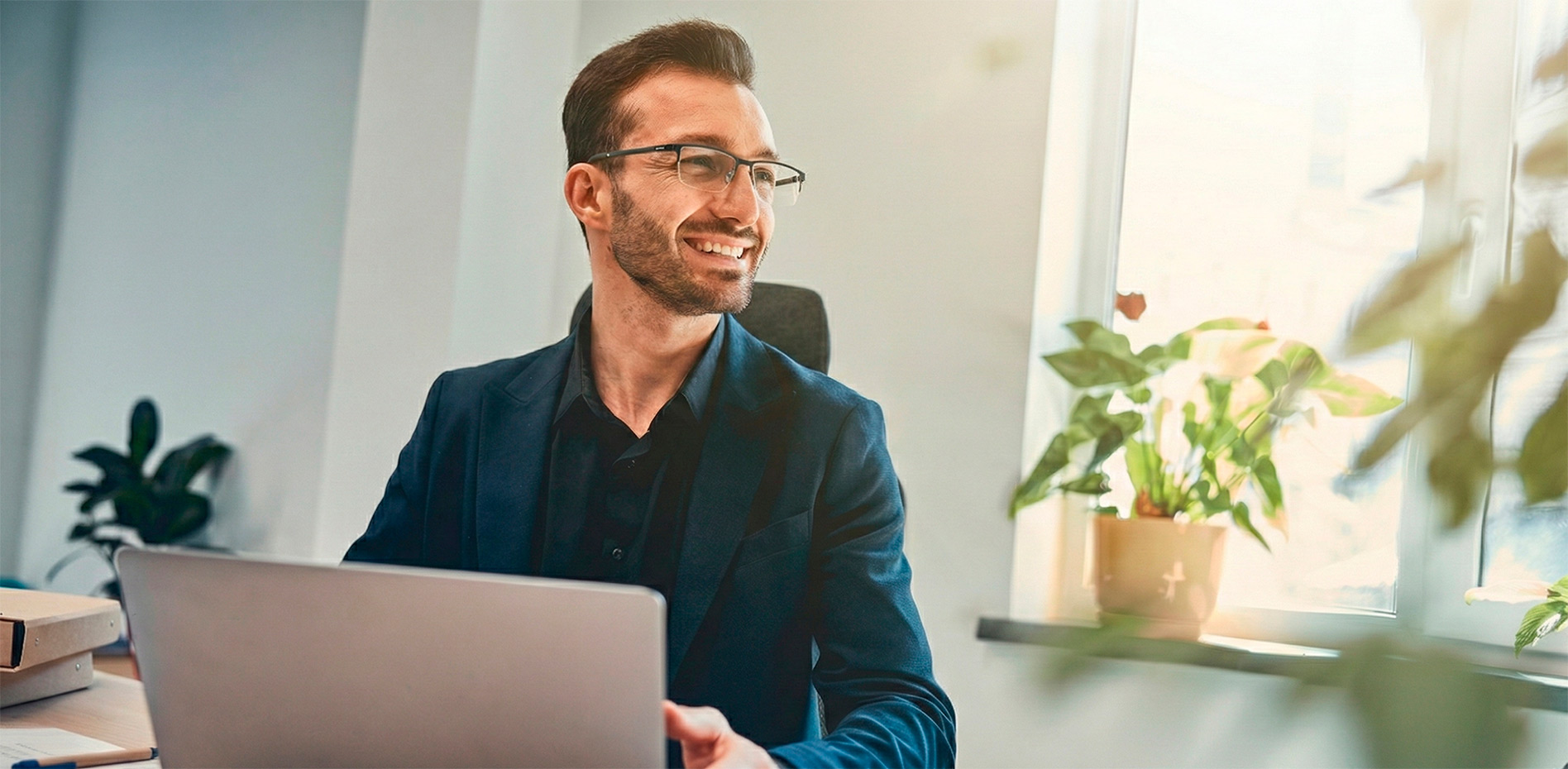 Profesional de gestión de proyectos sonriendo mientras trabaja con su laptop en una oficina iluminada, representando el éxito y la eficiencia en la ejecución de estrategias de innovación.
