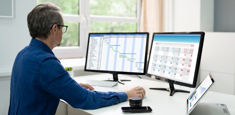 Profesional analizando simultáneamente un diagrama de Gantt y un calendario en monitores duales, optimizando la planificación y el seguimiento del tiempo en la gestión de proyectos de innovación empresarial.