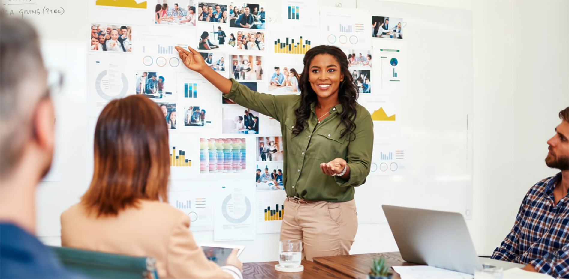 presentacion-analisis-datos-estrategia-corporativa-innk Una profesional sonriente presenta métricas y gráficos en una pizarra blanca llena de reportes visuales ante un equipo de trabajo en una oficina moderna.