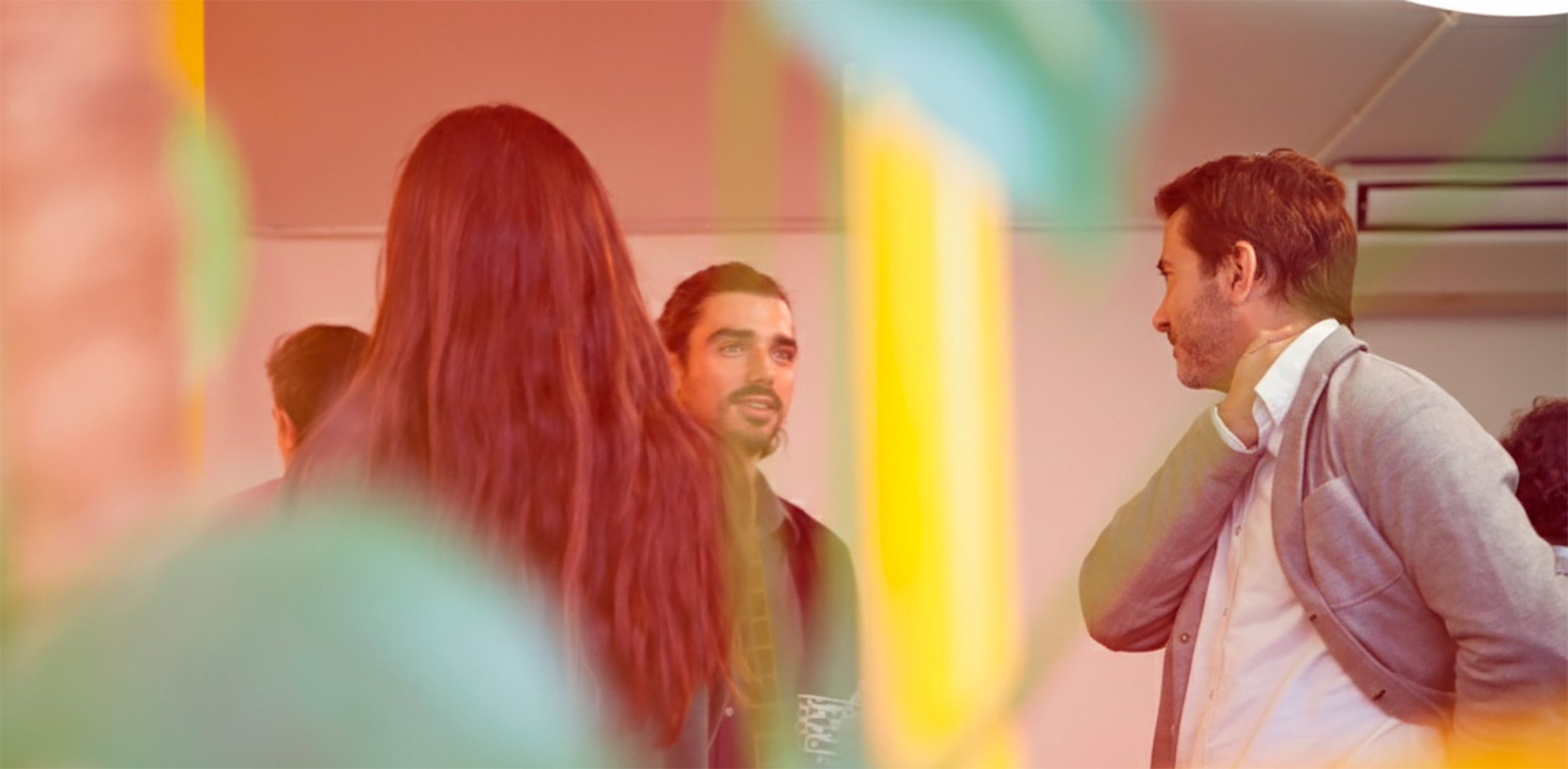 networking-colaboracion-equipo-oficina-innk Vista desenfocada a través de plantas de una oficina donde varios profesionales conversan y colaboran en un ambiente de trabajo dinámico.