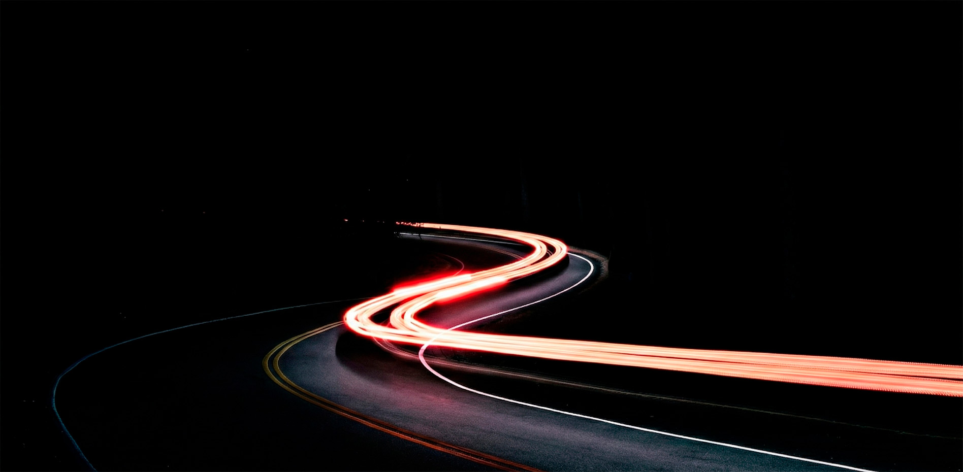 velocidad-innovacion-trayectoria-futuro-negocios-innk Estelas de luz roja en larga exposición siguiendo la curva de una carretera nocturna, representando conceptos de velocidad, innovación tecnológica y trayectoria empresarial.