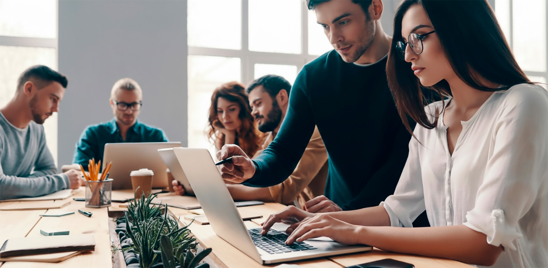 colaboracion-equipo-oficina-moderna-gestion-proyectos-innk Un equipo de profesionales trabaja en conjunto en una mesa de madera con laptops en una oficina luminosa, con un hombre señalando una pantalla mientras una mujer escribe.